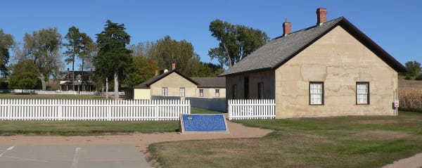Pale concrete buildings of Fort Hartsuff stand behind a white picket fence around the parade ground.