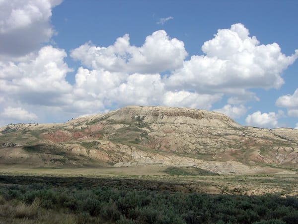 Fossil Butte, a flat-topped ridge banded in pale buff and red, above a sagebrush flat under tall summer clouds