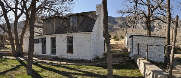 The two-story stone Frijole Ranch house and a small outbuilding shaded by bare trees at the foot of the Guadalupe Mountains.