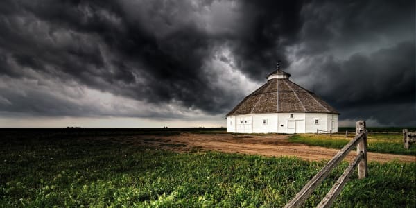 The white sixteen-sided Fromme-Birney barn under dark storm clouds, with green fields and a rail fence in front.