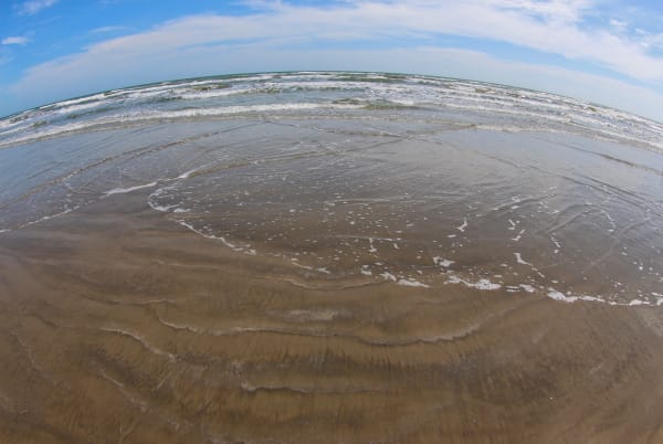 Shallow surf washing over a wide sand beach at Galveston Island State Park, seen through a fisheye lens.