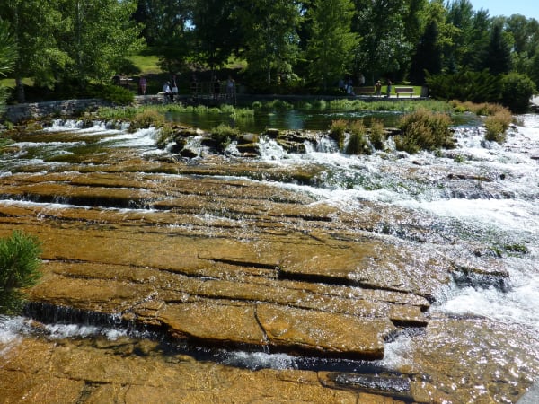 Clear spring water spilling over flat sandstone ledges at Giant Springs, green trees behind