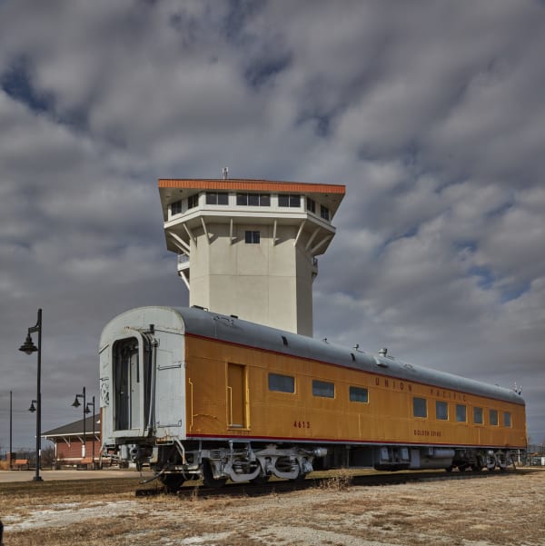 The Golden Spike Tower rises behind a yellow Union Pacific passenger car beside Bailey Yard in North Platte.