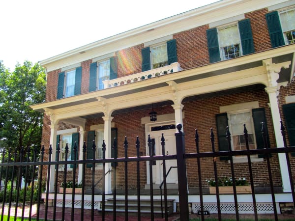 The red brick Harris-Kearney House with green shutters and a white columned porch behind an iron fence.
