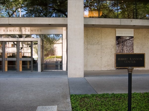 The glass entrance and stone walls of the Harry Ransom Center in Austin, with its name on a dark sign beside the door.
