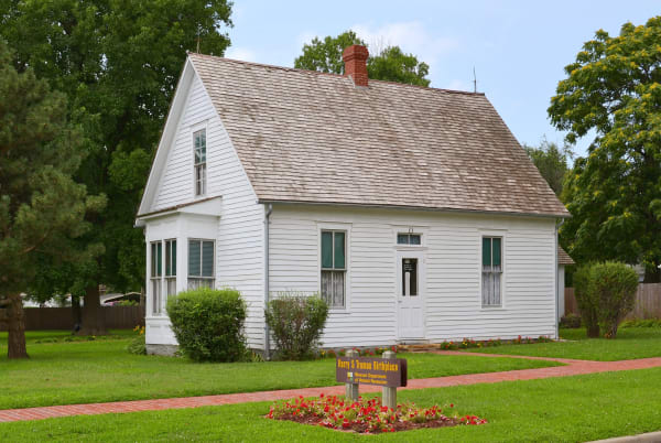 The small white frame house in Lamar where Harry S Truman was born, with a site sign and flower bed on the lawn.