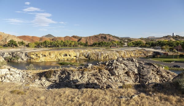 Orange and cream travertine terraces of Hot Springs State Park along the Bighorn River at Thermopolis, red hills and cottonwoods beyond
