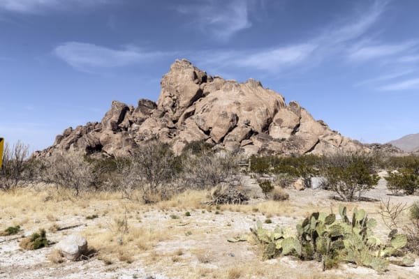 A tumbled mound of granite-like boulders rising above cactus and desert brush at Hueco Tanks State Park and Historic Site.
