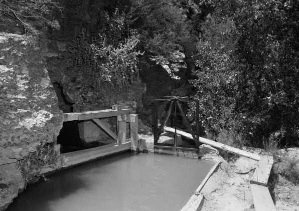 The concrete-lined Hurricane Canal running full of water into an opening cut in the cliffside in 1971, with timber control-gate frames standing over the channel