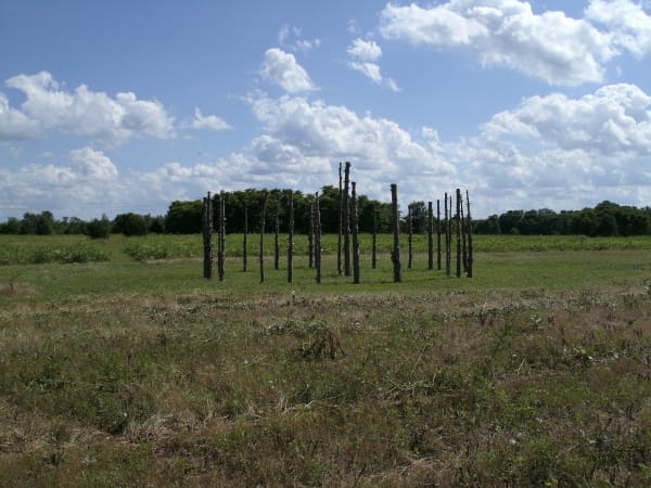 Wooden posts marking the outline of a lodge in the open grassland at Iliniwek Village State Historic Site.