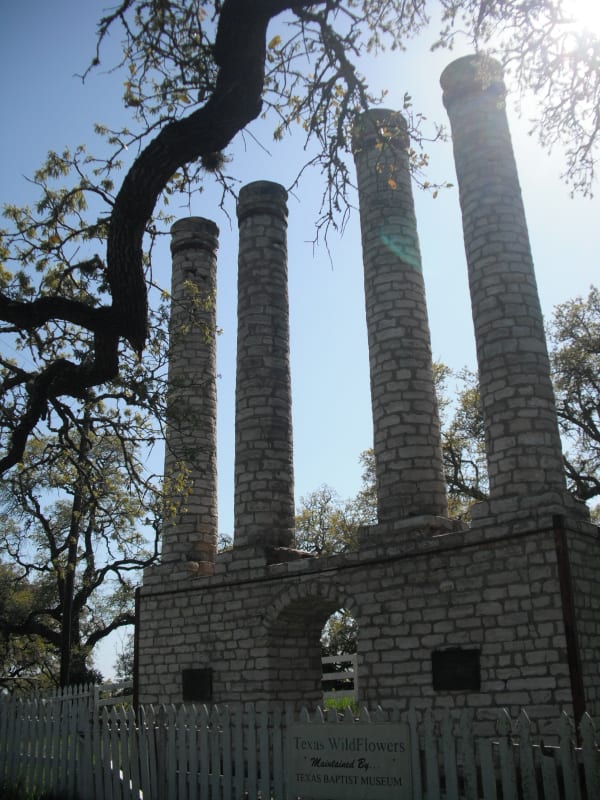 The four stone columns of the old Baylor Female College standing on a stone base under oak branches at Independence.