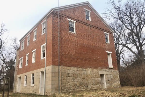 The three-story brick mission building on a stone ground floor near Highland, seen from the south among bare trees.
