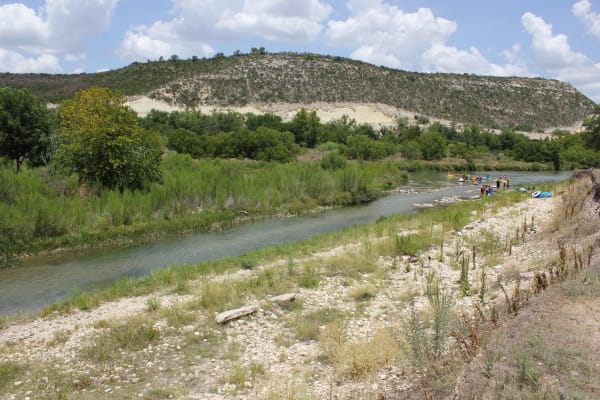 The South Llano River at Junction, running between gravel banks and green trees below a pale limestone bluff.