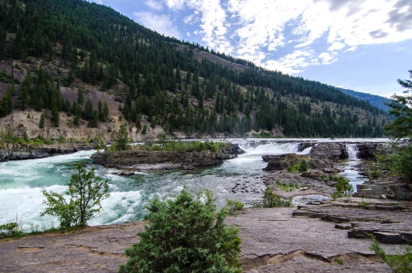 Kootenai Falls, the river breaking white over ledges of rock below forested hills