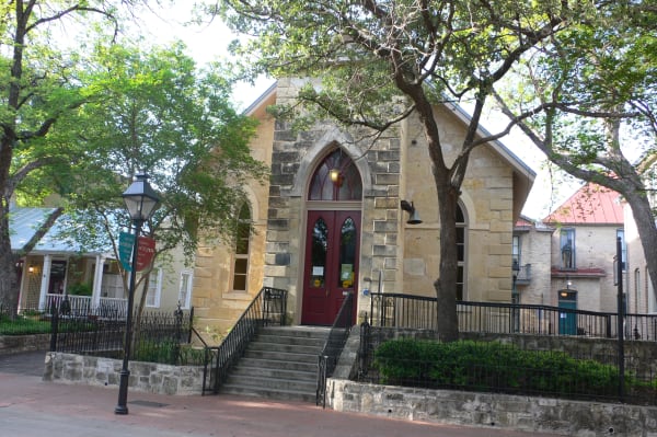 The limestone Little Church of La Villita in San Antonio, with its pointed arch doorway, iron railings and shade trees.