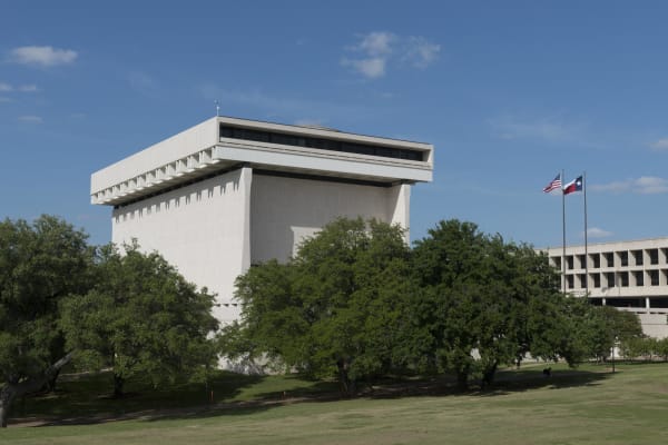 The windowless cream travertine block of the LBJ Presidential Library in Austin rising above green trees and lawn.