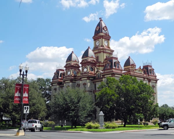 The Second Empire Caldwell County Courthouse in Lockhart, with its clock tower and mansard roofs above the square trees.