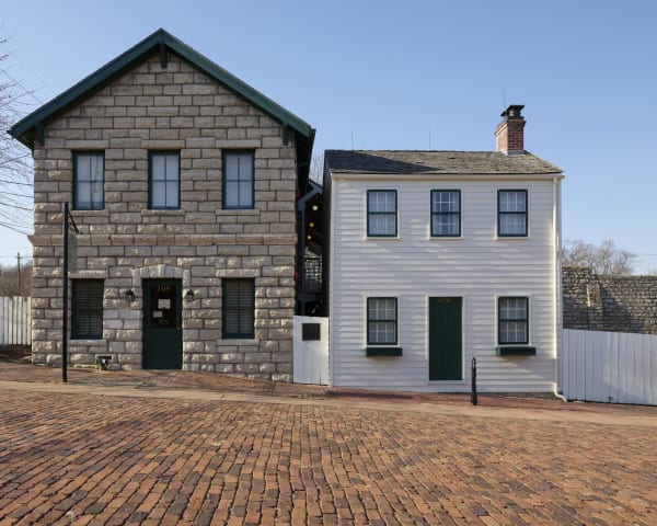 The white clapboard Mark Twain Boyhood Home beside the stone museum building on a brick street in Hannibal.