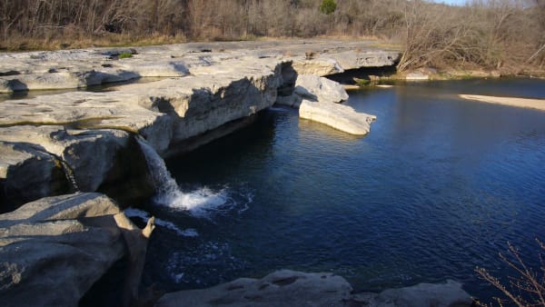 Onion Creek spilling over pale limestone ledges into a deep blue pool at McKinney Falls State Park in Austin.