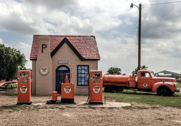 The small brick Phillips 66 cottage station in McLean with a steep red roof, three orange pumps and an old orange tank truck beside it.