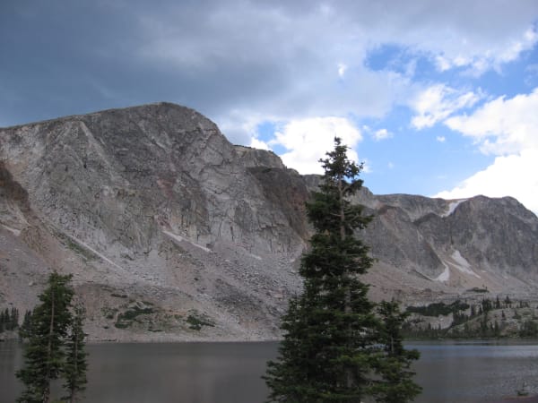 The pale quartzite face of Medicine Bow Peak rising above Lake Marie, spruce trees on the shore