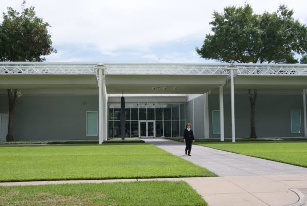 The long, low grey building of the Menil Collection in Houston, with a white steel canopy over the entrance and a lawn in front.