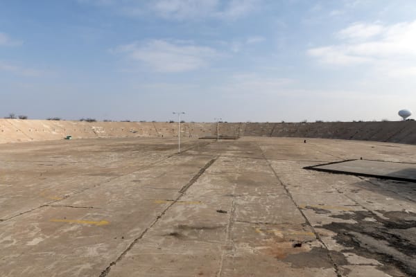 The cracked concrete floor and sloping earthen walls of the Million Barrel oil tank in Monahans, with a water tower on the horizon.