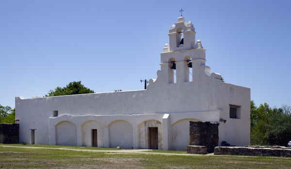 The white plastered church of Mission San Juan in San Antonio, with its pierced bell wall and a row of arched openings along the side.