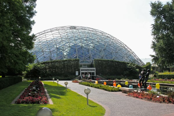 The geodesic glass dome of the Climatron rising behind flower beds and a curving path at the Missouri Botanical Garden.