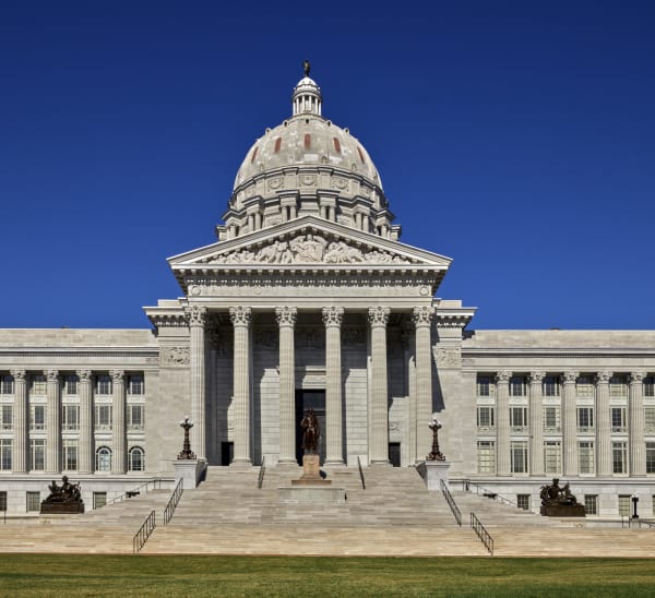 The domed limestone Missouri State Capitol and its columned portico and broad front steps under a deep blue sky.