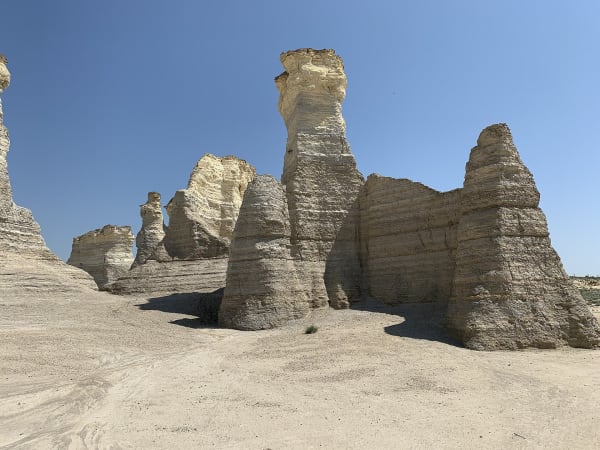 Tall weathered chalk spires of Monument Rocks standing on pale bare ground.