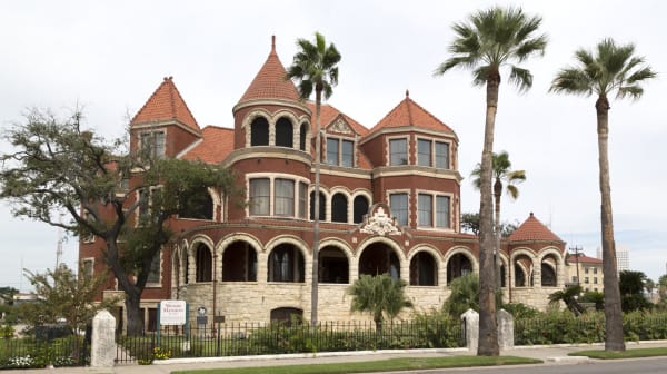 The four-story Moody Mansion in Galveston, red brick and stone with arched porches and turreted gables, among palm trees.