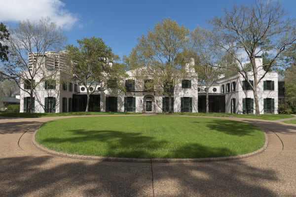 The pale stucco house at Bayou Bend, Ima Hogg's home in Houston, seen across a circular lawn and drive under tall trees.