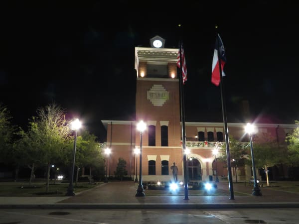 Navasota City Hall at night, a brick building with a lit clock tower beside flagpoles flying the United States and Texas flags.