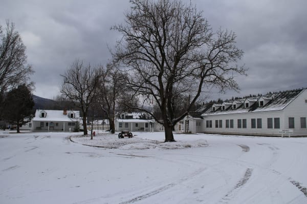 White Cape Cod-style buildings of the Ninemile Remount Depot around a snow-covered drive, bare trees against a grey sky