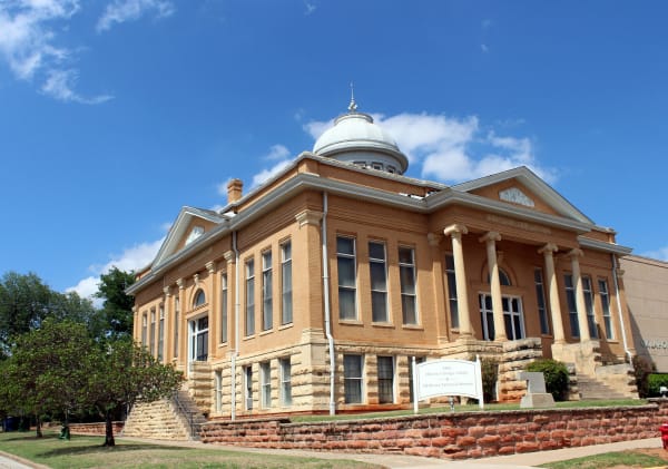 The domed 1902 Carnegie Library in Guthrie, a buff brick building with a columned portico, behind a sign for the Oklahoma Territorial Museum.