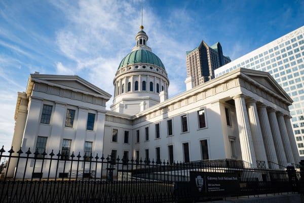 The white columned Old Courthouse and its green copper dome against a blue sky in downtown St. Louis.