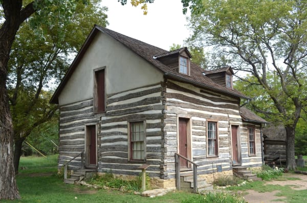 The Darius Sales Munger House at Old Cowtown Museum, a weathered log-and-plaster house with dormer windows under shade trees.