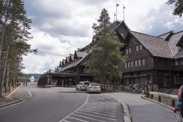 The Old Faithful Inn, a long log and shingle building under a steep roof with dormers, lodgepole pines along the drive in front