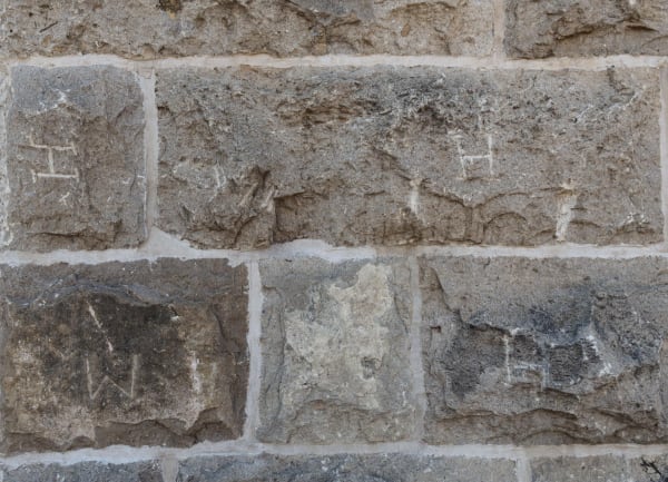 Rough-cut limestone blocks in a wall of the Old Jail Art Center in Albany, several cut with letters such as H and W that the masons carved to claim their work.