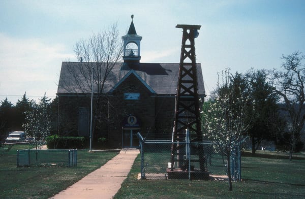 The stone Osage Nation Museum building in Pawhuska with an oil derrick beside the walk.