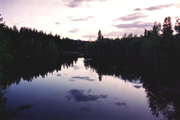One of the Payson Lakes at dusk — still dark water holding an almost unbroken reflection of the spruce and aspen ringing it, the far shore low and wooded, and a mauve and cream sky with broken cloud standing above the treeline.