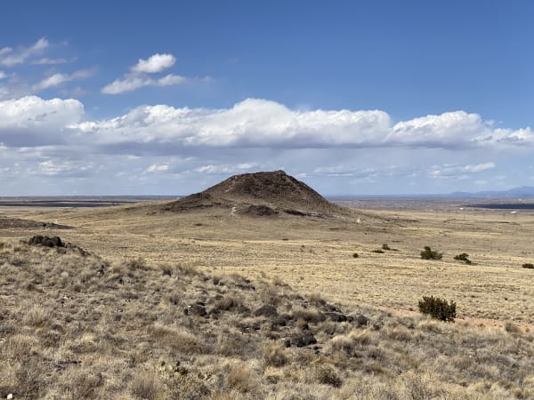 The dark cone of Vulcan Volcano rising from dry grassland on Albuquerque's West Mesa, seen from the volcanoes trail