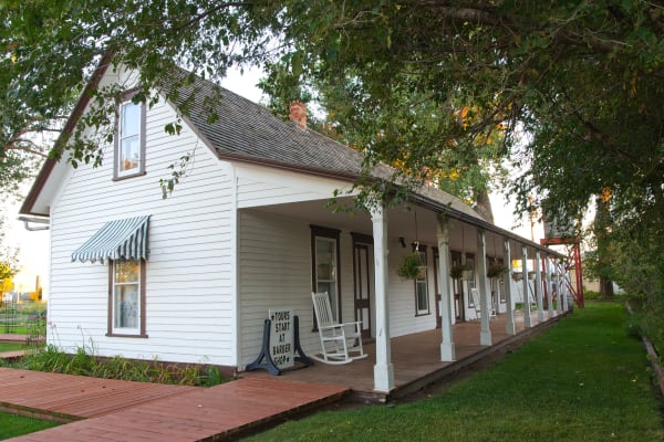 The Pierre Wibaux House, a white clapboard building with a long shaded porch and rocking chairs, under green trees