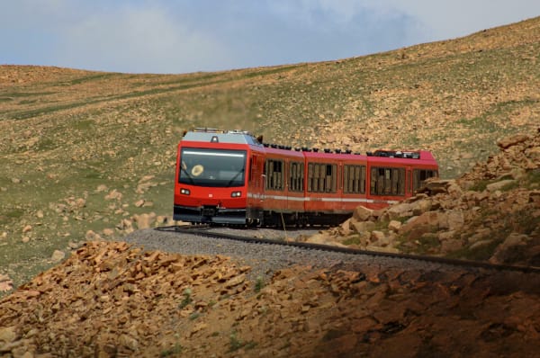 A red Pikes Peak Cog Railway train climbing above timberline near the summit