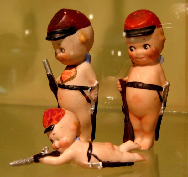 Three small Kewpie doll figures in red caps and belts in a display case at the Ralph Foster Museum.