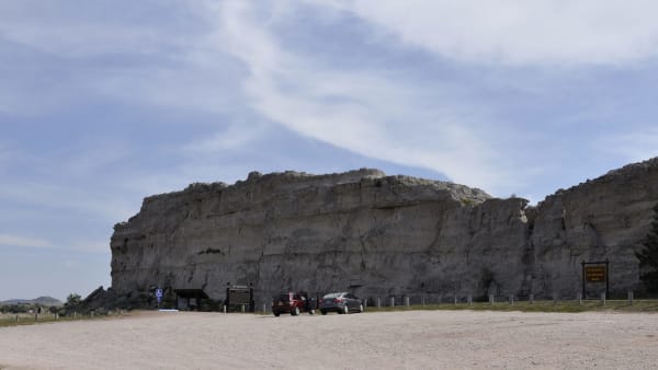 Register Cliff, a long pale sandstone bluff above a gravel parking area near Guernsey, a few cars at its foot