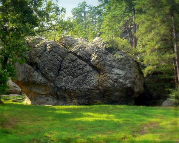 A great tilted sandstone boulder above green grass among pines and oaks at the Robbers Cave trailhead.