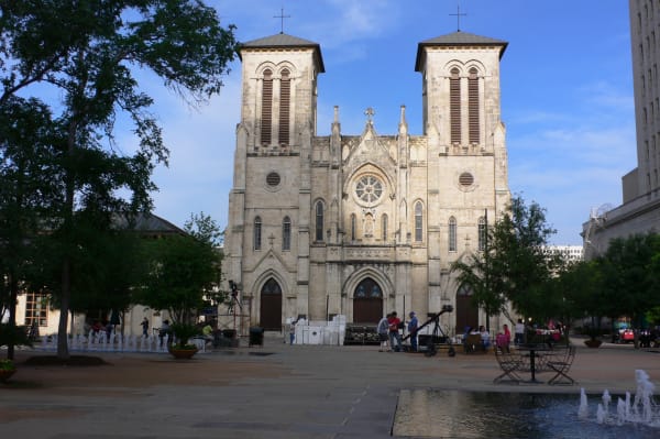 The pale stone Gothic Revival front of San Fernando Cathedral in San Antonio, with twin towers and a rose window above Main Plaza.
