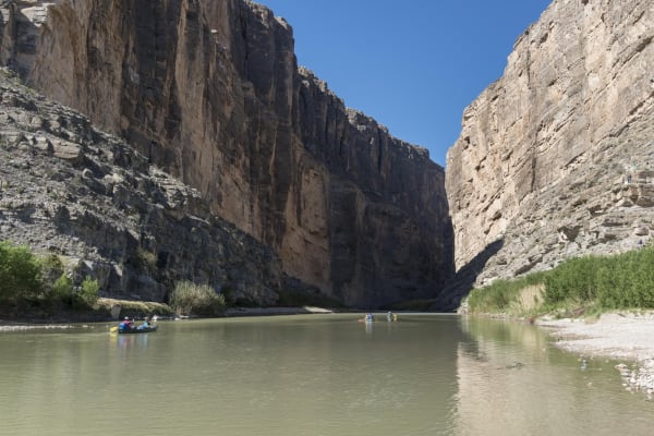The Rio Grande flowing out of Santa Elena Canyon between sheer limestone walls, with paddlers on the water.
